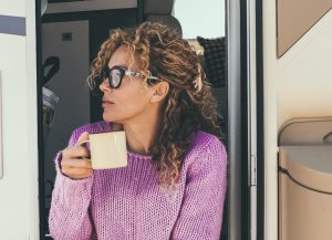 Woman drinking coffee sitting at the door of an rv camper