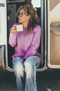 Woman drinking coffee sitting at the door of an rv camper