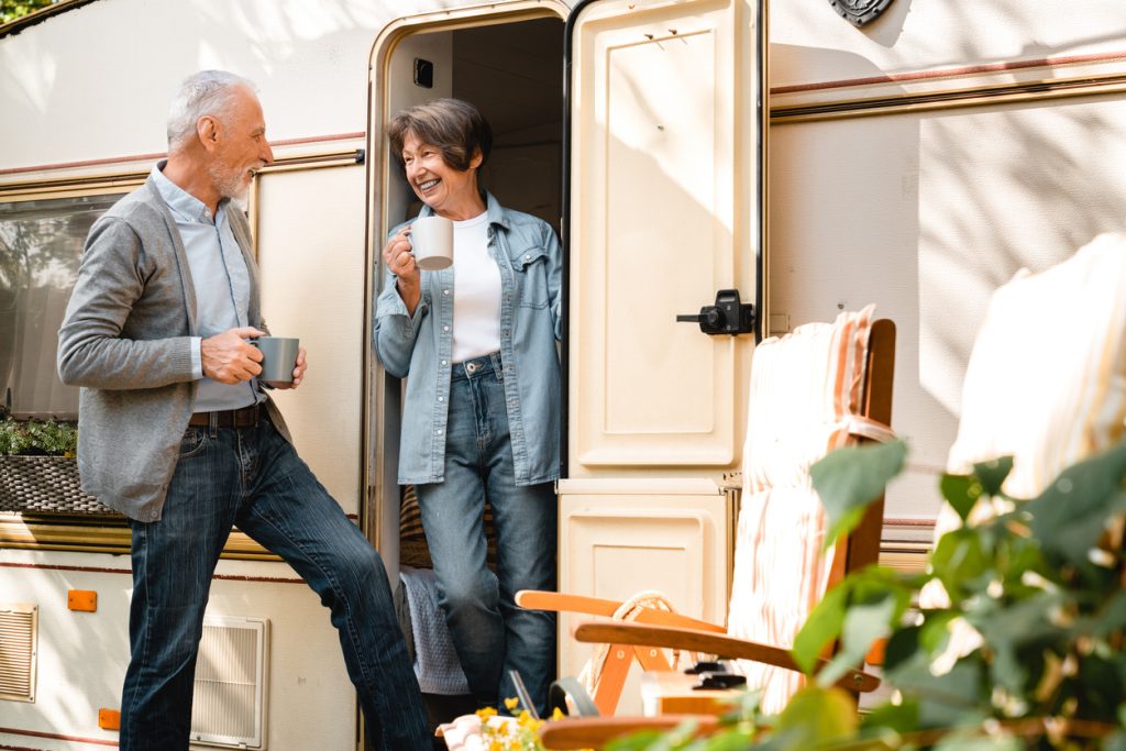 Active old senior elderly caucasian couple spouses husband and wife having breakfast on the porch of trailer camper van motor wheel home. Caravanning grandparents, eco-tourism